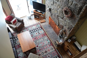 A cozy living room with a stone fireplace, a leather armchair, a wooden coffee table, and a patterned rug. - Slopeside Family Ski in, ,Wifi, Hot Tub, Pool, Yellowstone, Netflix (Teton Village)