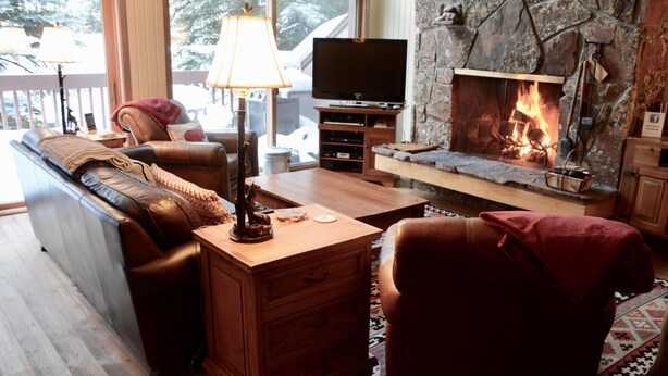 Un salón acogedor con chimenea, sofá de cuero, mesa de centro de madera y televisor sobre un mueble.