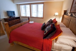 A bedroom with a wooden bed, a television on a dresser, and a window with blinds. - Slopeside Family Ski in, ,Wifi, Hot Tub, Pool, Yellowstone, Netflix (Teton Village)