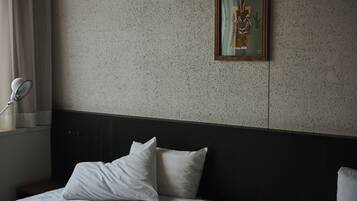 A hotel room with a bed, pillows, a headboard, a wall-mounted picture, and a window with curtains.