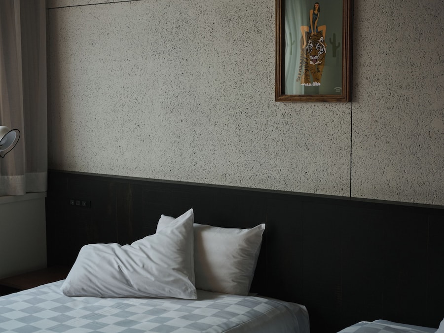 A hotel room with a bed, pillows, a headboard, a wall-mounted picture, and a window with curtains.