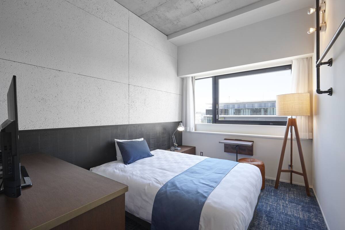 Une chambre d’hôtel avec un lit, un bureau, une lampe et une fenêtre donnant sur un paysage agréable.