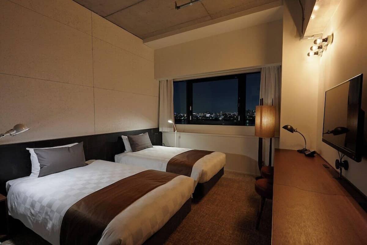 Une chambre d’hôtel avec deux lits, un bureau, une télévision et une fenêtre donnant sur la ville.