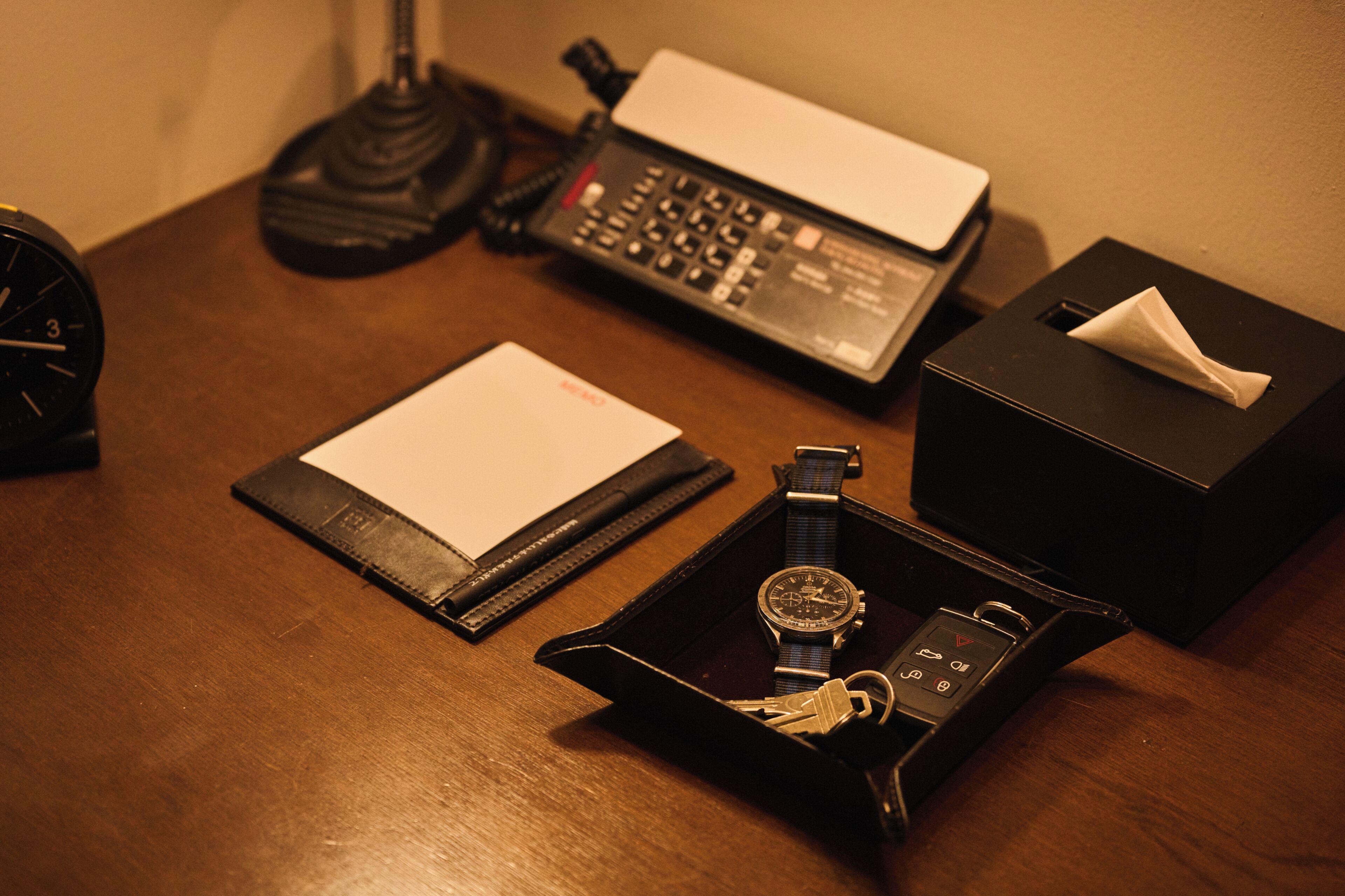 A desk with a watch, a notepad, a telephone, and a tissue box.