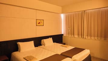 A hotel room with two beds, a headboard, a framed picture, a window with curtains, and a bedside table.
