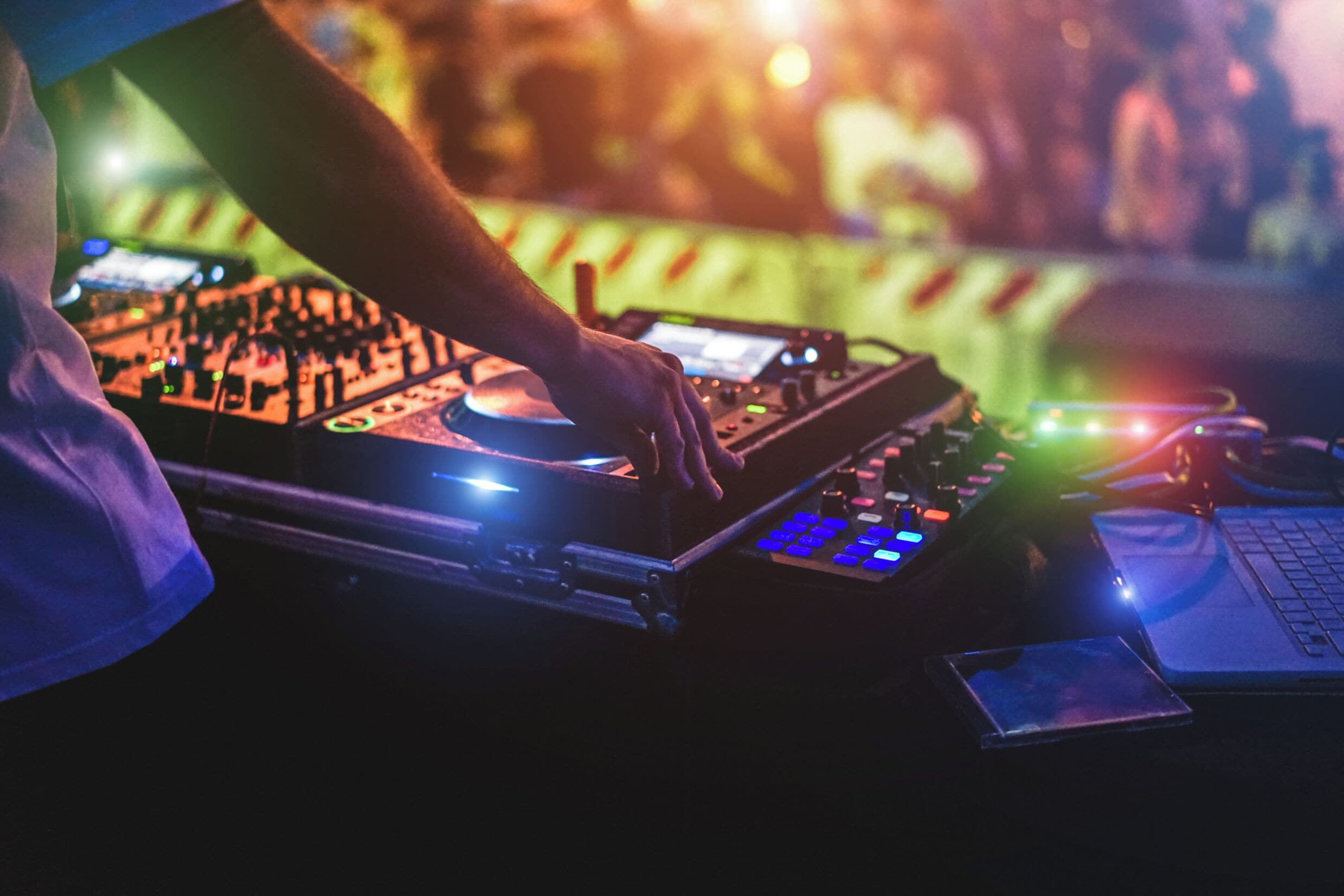 A person operating DJ equipment with a laptop and a mobile device on a table.