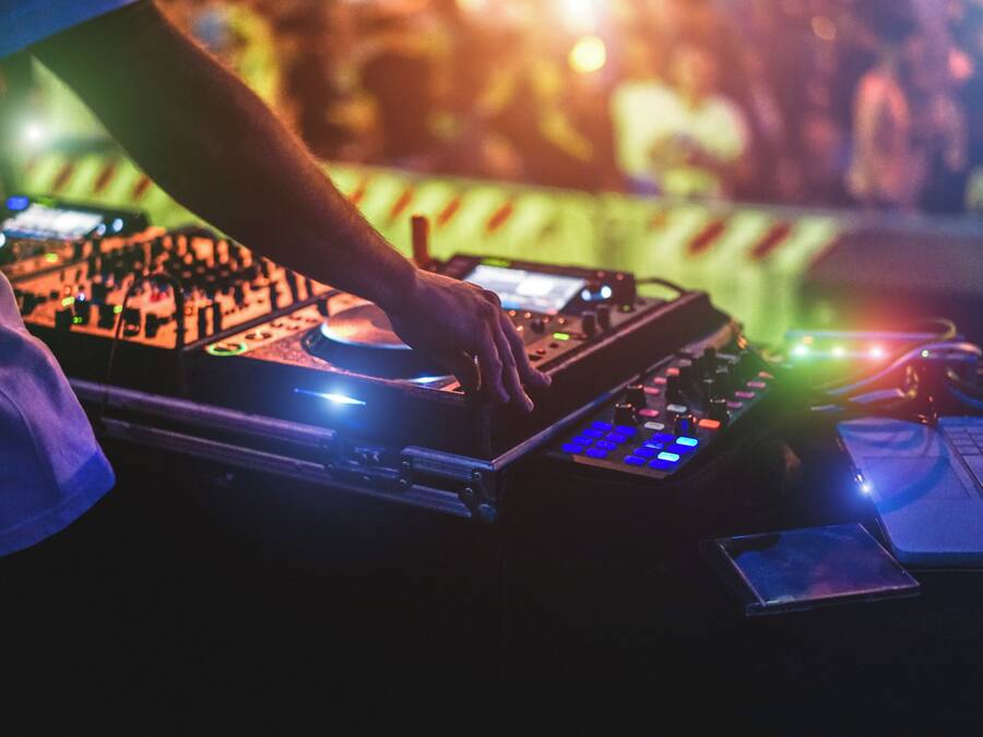Uma pessoa a manipular equipamento de DJ, com um laptop e um dispositivo móvel sobre uma mesa.