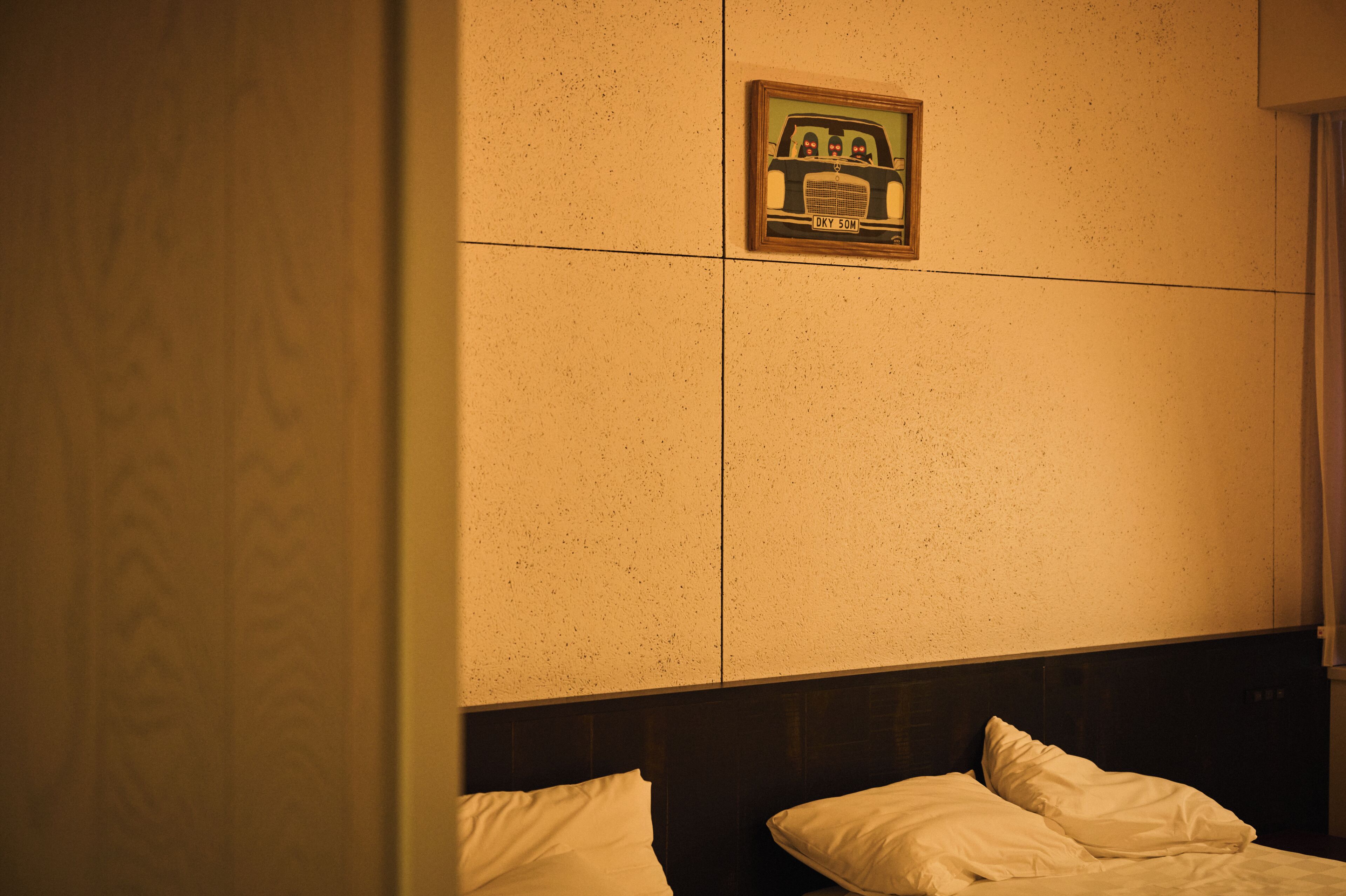 A hotel room with a bed, a headboard, and a wall-mounted picture.