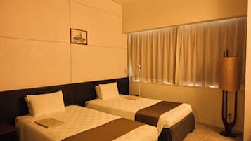 Quarto de hotel com duas camas, janela com cortinas, luminária na parede e uma pequena fotografia.