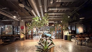 An indoor space with a central plant, seating areas, and a visible exit door. - The HOTEL Well-hub Haneda (Kawasaki)