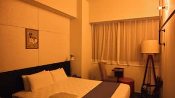A hotel room with a bed, a nightstand, a lamp, a chair, a window with curtains, and a wall-mounted picture.