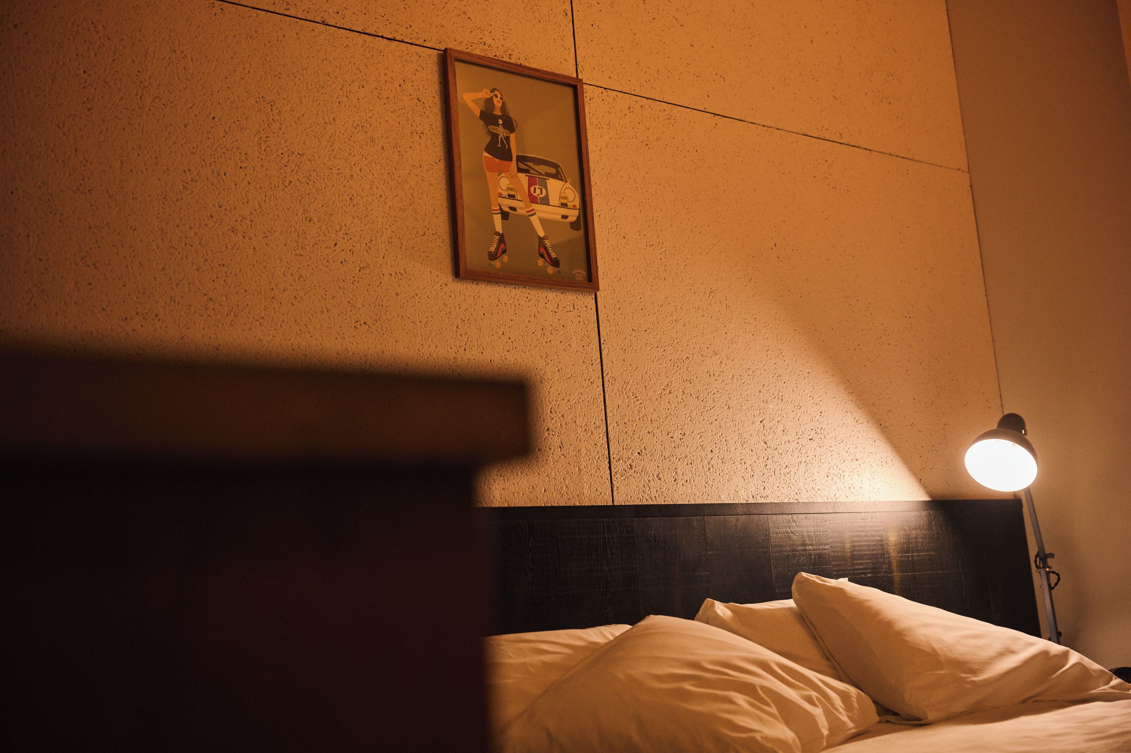 A hotel room with a bed, a nightstand, a framed picture on the wall, and a floor lamp.
