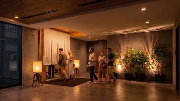 A modern hotel lobby with a wooden ceiling, a reception desk, and potted plants.