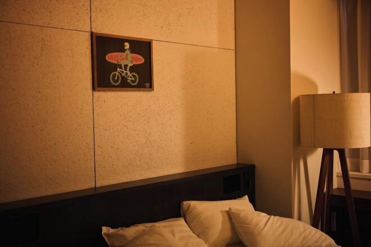 A hotel room with a bed, a wall-mounted picture of a person on a bicycle, and a standing lamp.