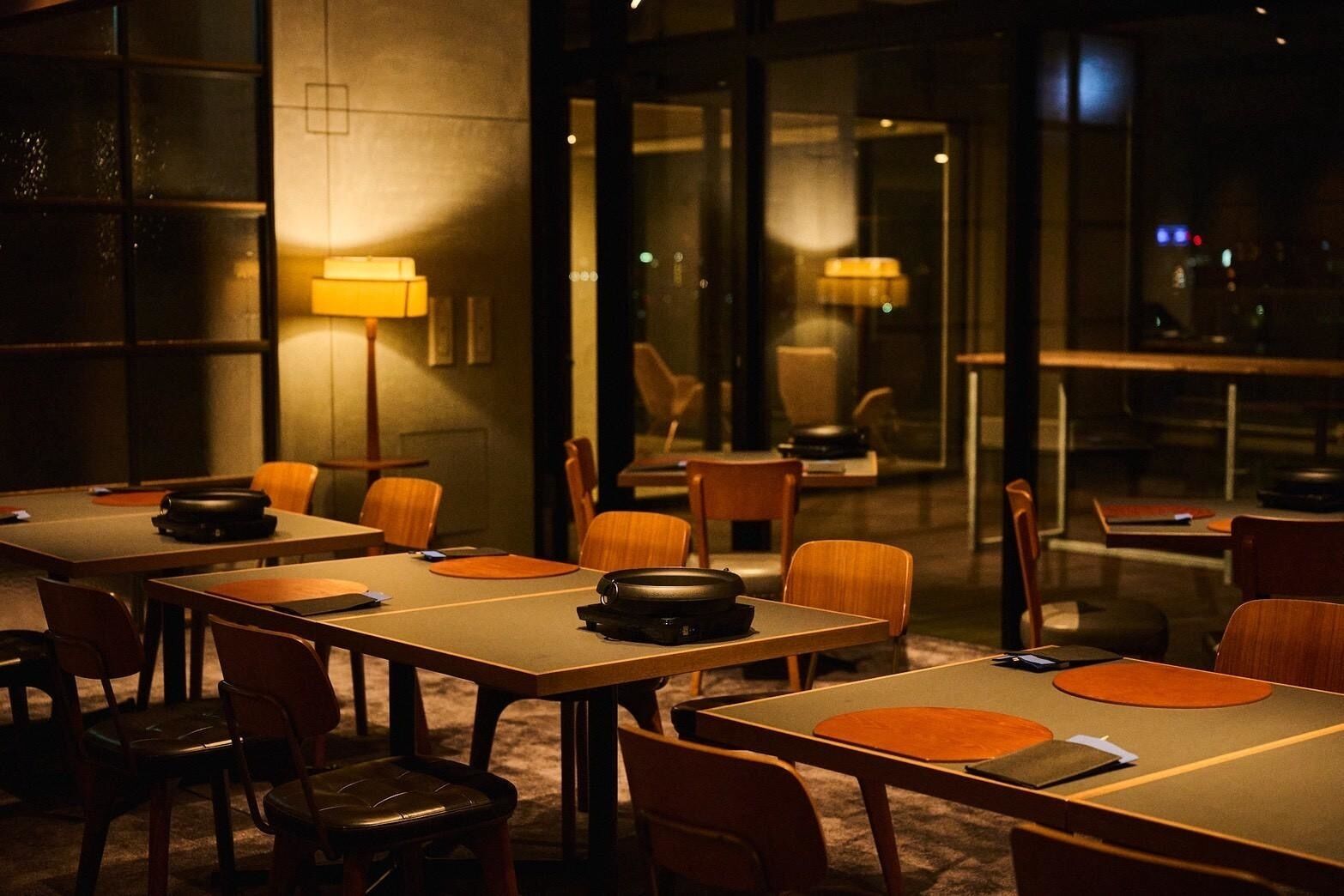 A hotel room with multiple tables and chairs, a lamp, and a view through a glass door.