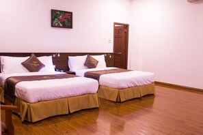 Habitación de hotel con dos camas, cada una con cabecero marrón y cubrecamas a juego. El suelo es de madera y hay una puerta a la derecha.