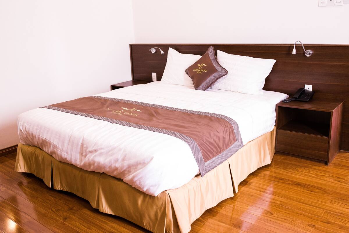 A neatly made bed with a brown headboard, a bedside table with a phone, and a wall socket.