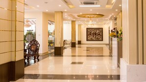 A spacious lobby with a polished floor, elegant chandeliers, and a decorative wall piece. - Bazan Xanh Hotel (Buon Ma Thuot)