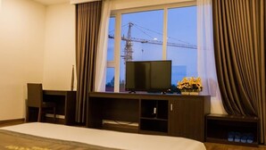 A hotel room with a bed, a desk with a TV, and a window with curtains. - Bazan Xanh Hotel (Buon Ma Thuot)