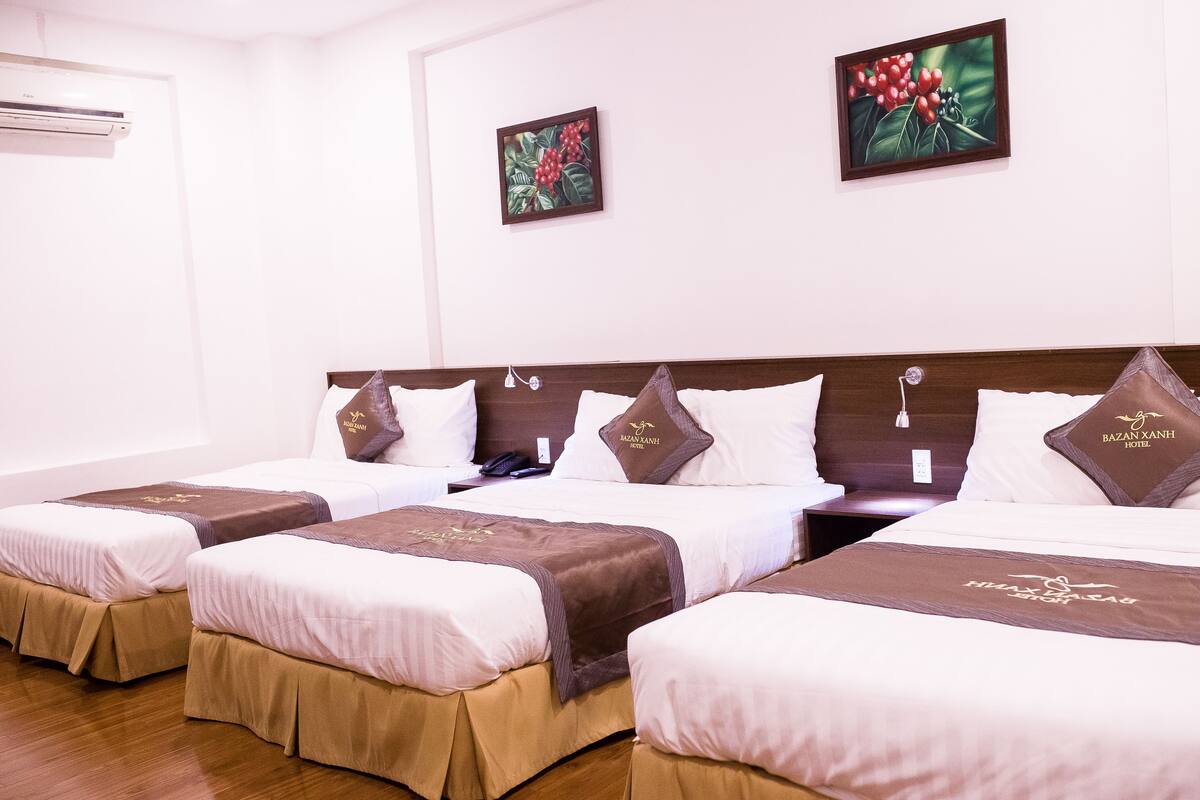 A hotel room with four beds, each with a brown headboard and white bedding. There are two wall-mounted air conditioners and two framed artworks above the beds.