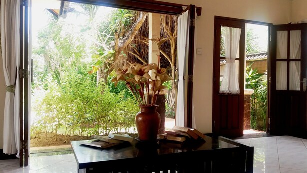 A room with a table, a vase with dried flowers, and a view of greenery outside. - Vantage Point Villas (Ungasan)