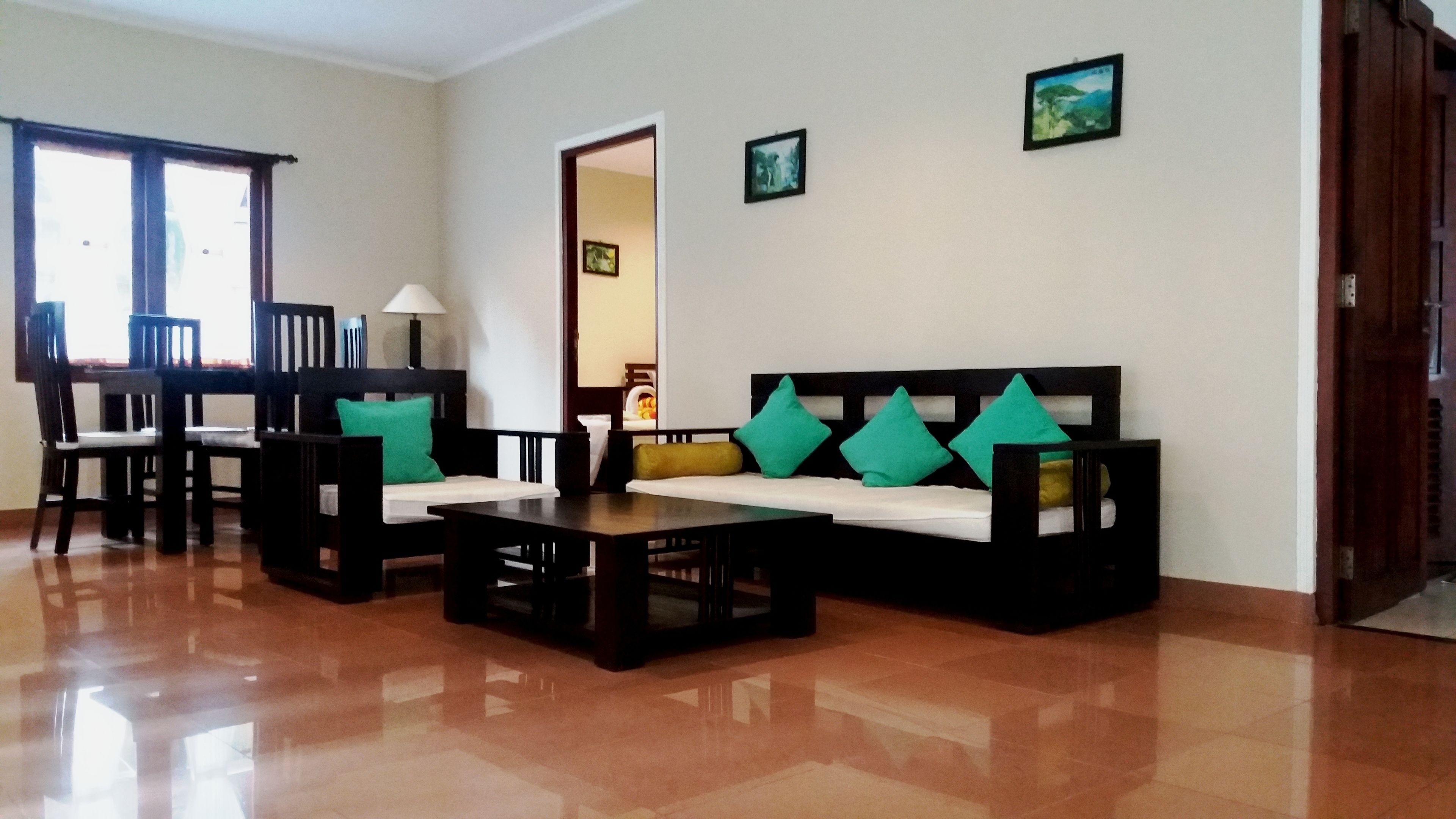 A living room with a sofa, chairs, a coffee table, and a dining table. There are two windows and a door.
