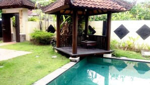 A pool area with a wooden gazebo, a small table, and a stone wall with diamond patterns. - Vantage Point Villas (Ungasan)