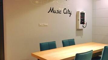 A conference room with a wooden table and teal chairs, a wall-mounted device, and a sign reading "Formosa Boulevard Music City".