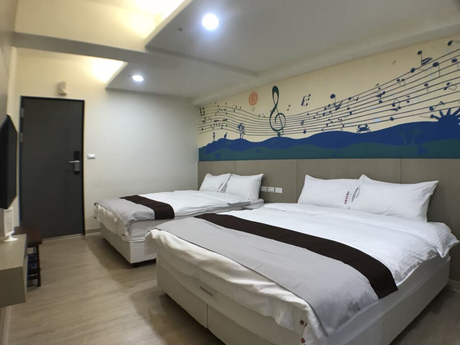 A hotel room with two beds, a large wall mural, and a TV on the left.