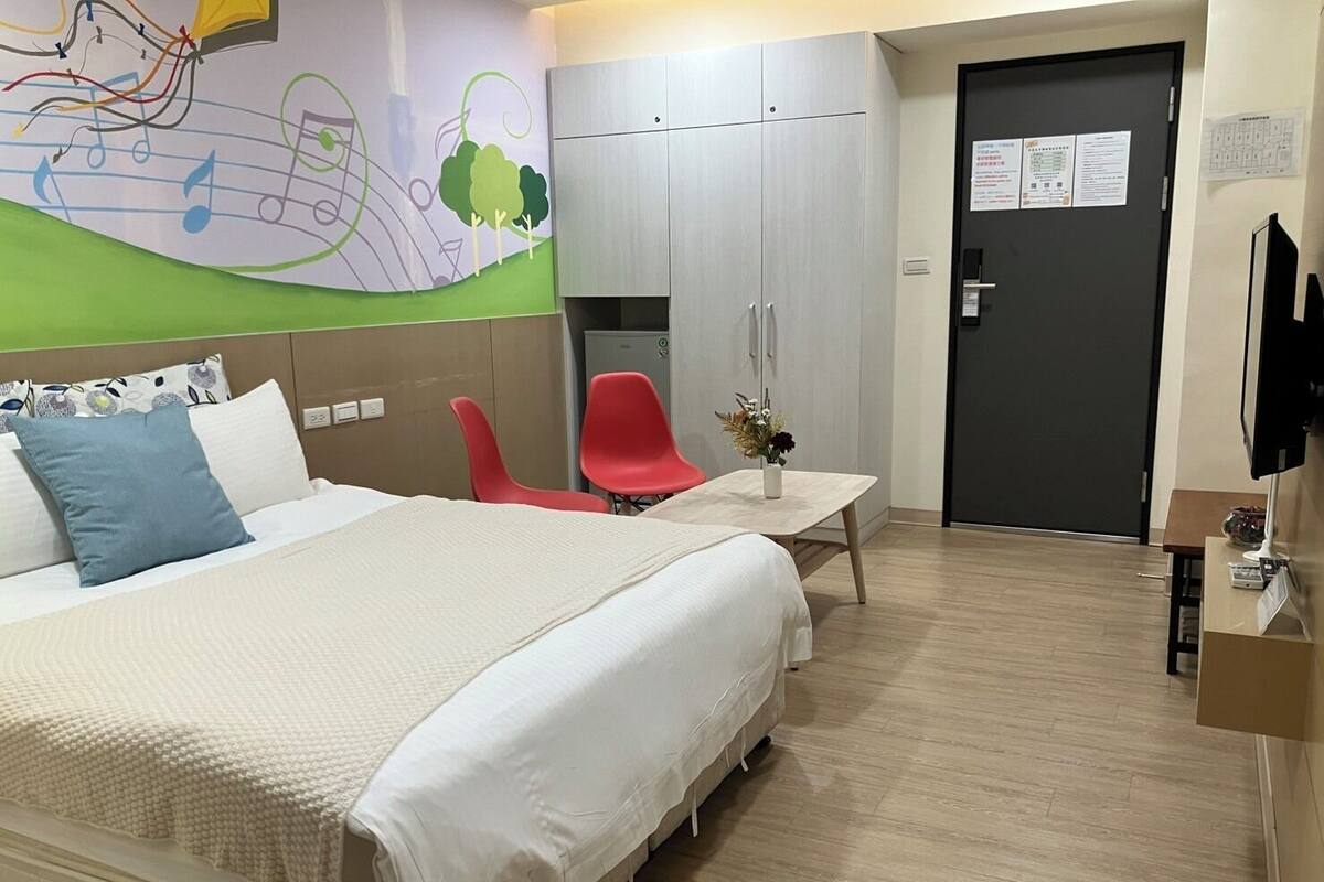 A hotel room with a large bed, a desk, a chair, and a wardrobe.