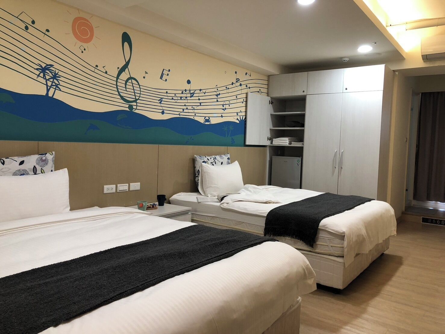 A hotel room with two beds, a wardrobe, a desk, and a wall mural.