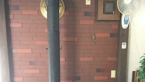 A wood-burning stove with a chimney, a fan, and a brick wall. - Kitashiga Lime Light (Yamanouchi)