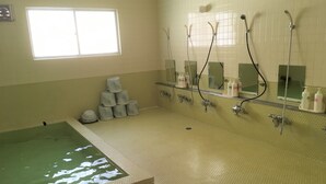 A bathroom with a large bathtub, a shower area with multiple faucets, and a window providing natural light. - Kitashiga Lime Light (Yamanouchi)