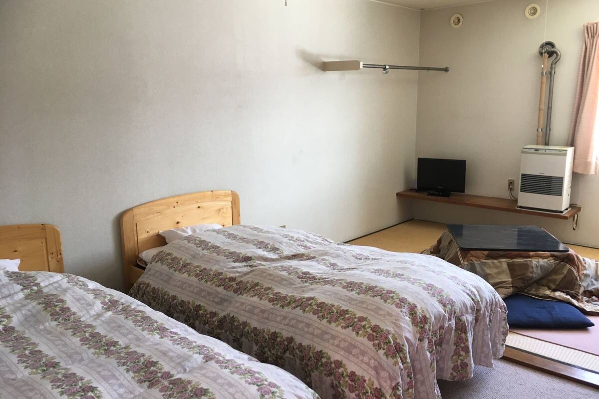 A bedroom with two wooden beds, a small TV, an air conditioner, and a window with curtains.