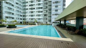 Ein Schwimmbecken mit Holzterrasse, umgeben von einem Hochhaus mit Balkonen.