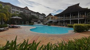 Una piscina rodeada de sillas de descanso y un edificio con techo tradicional.