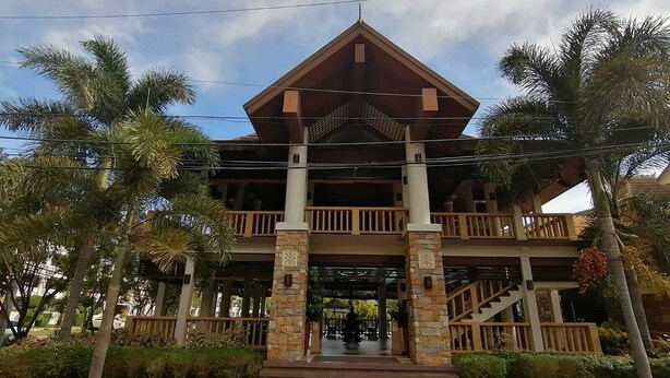 Un edificio de dos plantas con un atrio central, rodeado de palmeras y un césped cuidado.
