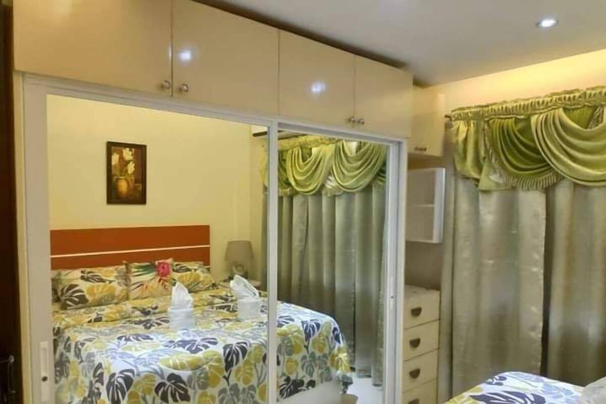 Quarto de hotel com cama, guarda-roupa, espelho e cortinas.