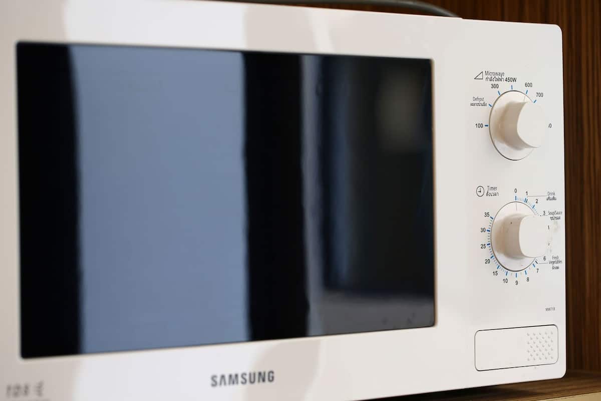 A white Samsung microwave with a digital display, a defrost setting knob, and a timer knob.