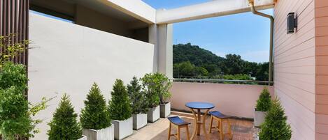 Un patio moderno al aire libre con una mesa redonda y dos sillas, rodeado de plantas en macetas y vistas a una ladera.