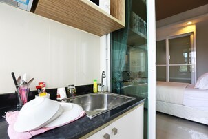 Una cocina moderna con un lavamanos de acero inoxidable, un área de comedor con una mesa y sillas blancas, y un dormitorio con cama y ventana.