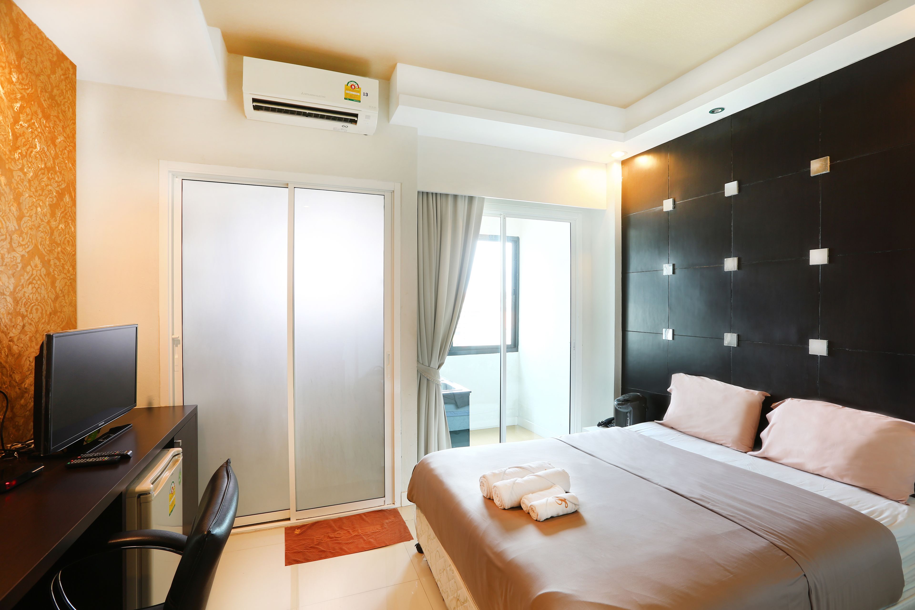 Habitación de hotel con cama, escritorio con televisor, una silla y equipo de aire acondicionado.