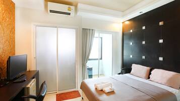 Habitación de hotel con cama, escritorio con televisor, una silla y equipo de aire acondicionado.