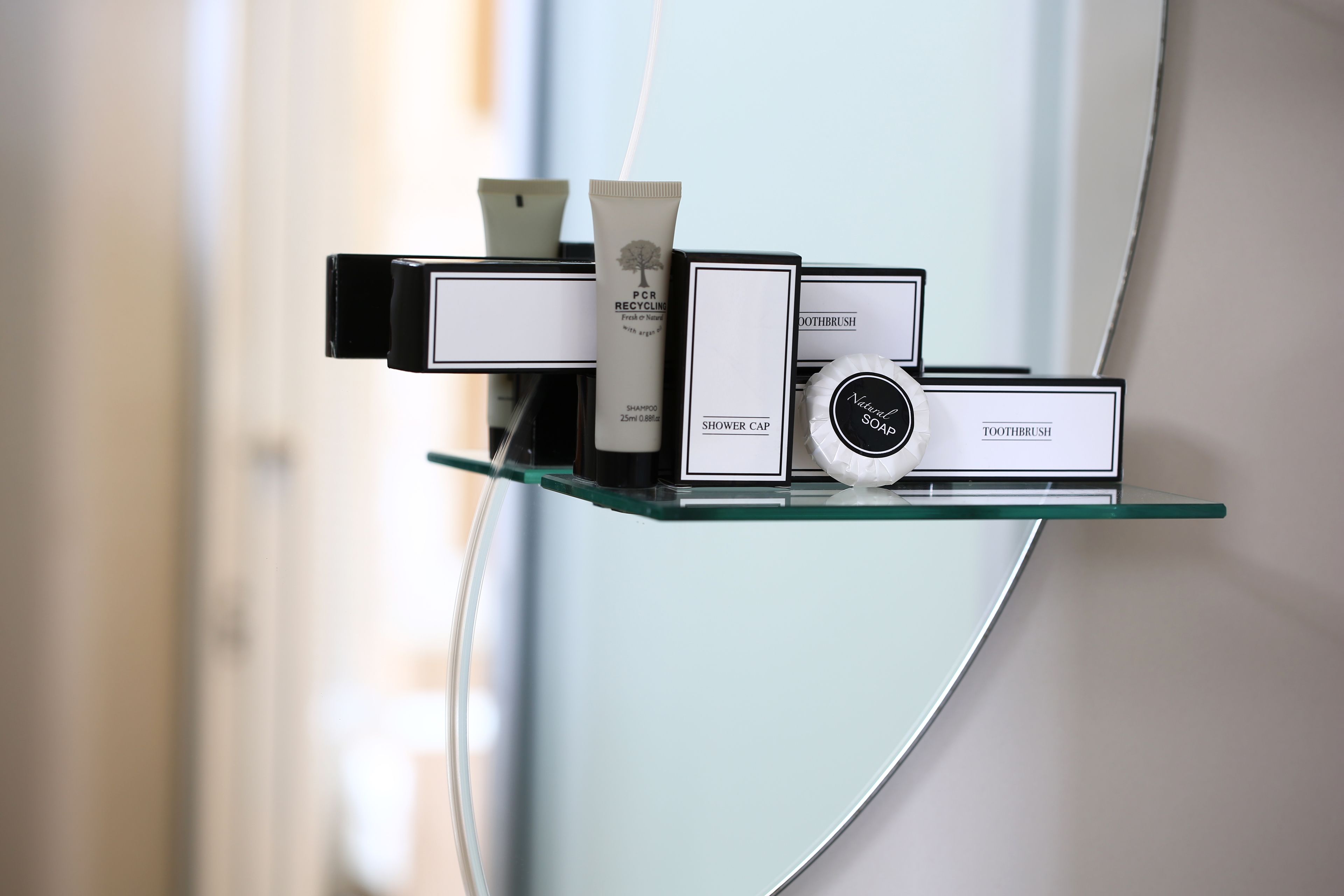 A glass shelf with toiletries including a shower cap, toothpaste, and a soap dispenser.