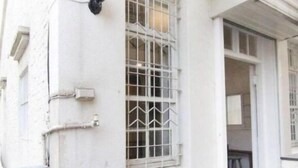 A white building with a window featuring a white grid pattern, a black wall-mounted light fixture, and a wooden deck. - Tainan Travel Inn (Tainan)