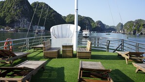 A boat deck with lounge chairs, a white umbrella, and a view of a mountainous coastline. - Cat Ba Sisters Legend Cruise (Hai Phong)