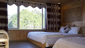 A room with two wooden beds, a wooden chair, a large window with curtains, and a view of a mountain. - Cat Ba Sisters Legend Cruise (Hai Phong)