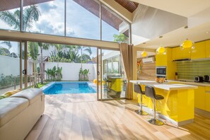 Una cocina moderna con armarios amarillos, una isla grande con taburetes y vistas a una piscina.