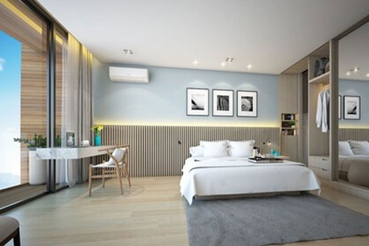 A modern hotel room with a bed, desk, chair, and large windows.