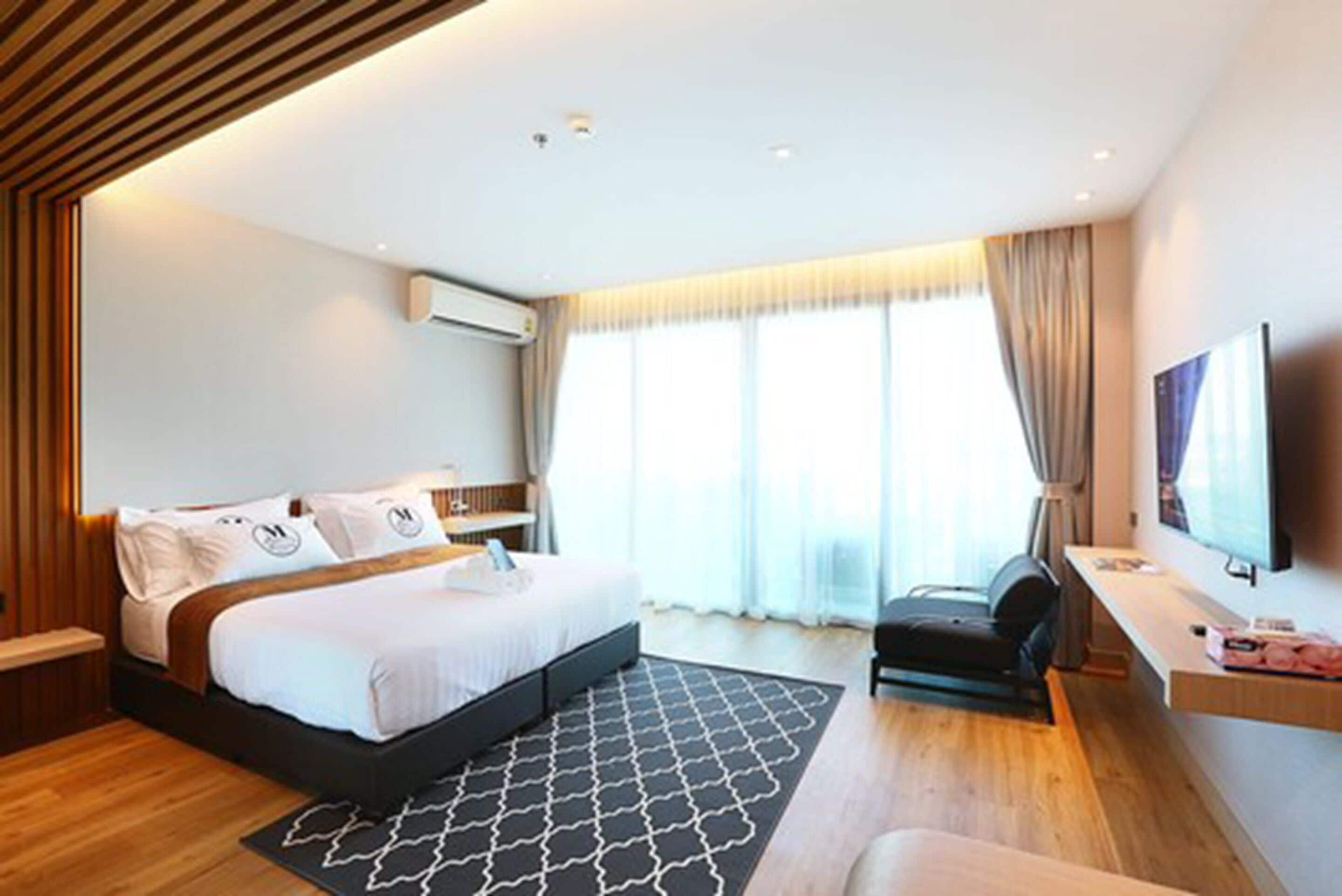 Una habitación de hotel moderna con una cama grande, un escritorio, un televisor y una ventana con cortinas.